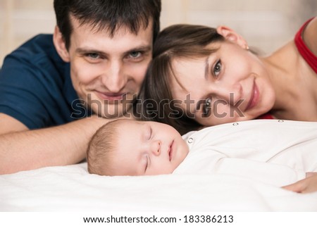 Smiling young couple and a little baby sleep in bed at home