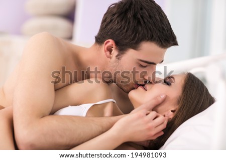 Loving couple in bed. Beautiful young loving couple lying in bed and kissing