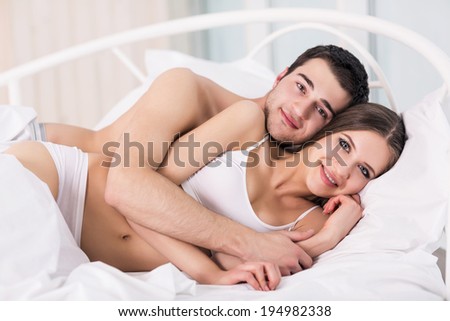 Loving couple in bed. Beautiful young couple lying in bed and looking at the camera