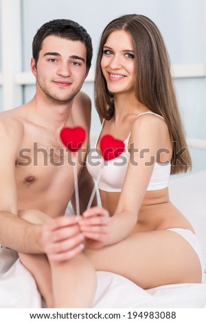 love valentine day couple holding red heart young lovely together lying in a bed, happy smile looking at camera, concept hearts flying around