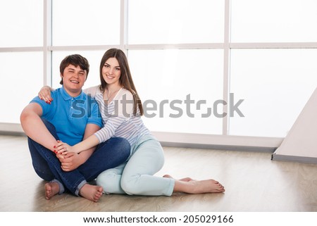 Attractive young adult couple sitting close on floor in home smiling and laughing.