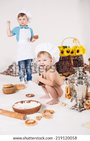 Cute kids, adorable little girl and funny boy wearing chef hats playing with dough baking a pie in a sunny white kitchen