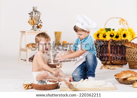 Cute kids, adorable little girl and funny baby boy wearing chef hats playing with dough baking a pie in a sunny white kitchen