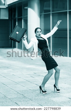 Scared young businesswoman with briefcase and gesturing fear on city background