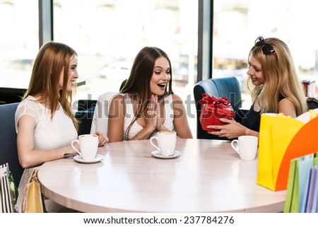 Cheerful young woman surprising friend with a gift in cafe