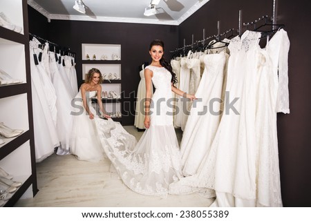 Smiling pretty bride chooses white gown at shop of wedding fashion