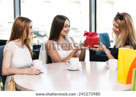 Cheerful young woman surprising friend with a gift in cafe