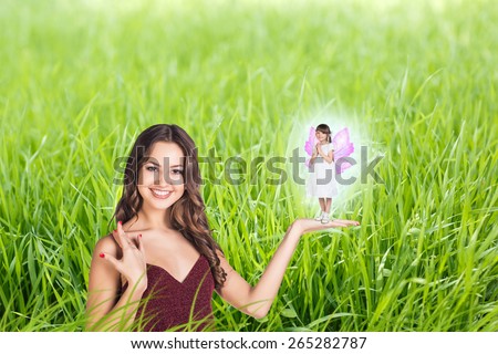 Beautiful woman with little girl with fairy wings on green grass background