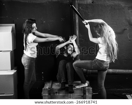 Two young women beaten man sitting on the box in basement on black-and-white background