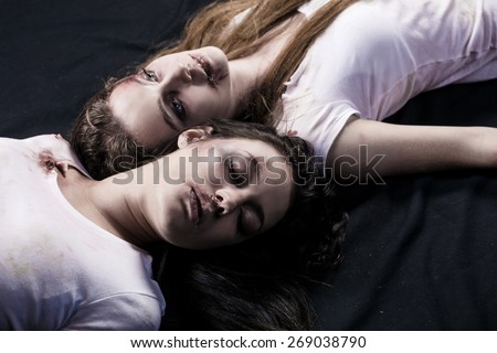 Two young beaten women with cuts and bruises lie down on the floor on black background