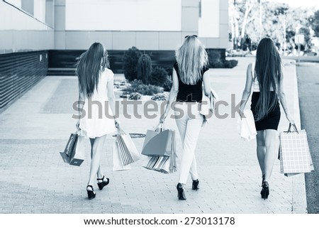 Girls holding shopping bags and walk around the shops. Smiling girlfriends having fun together