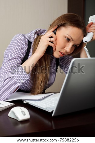 A stressed business woman tired as she tryes to answer two telephones