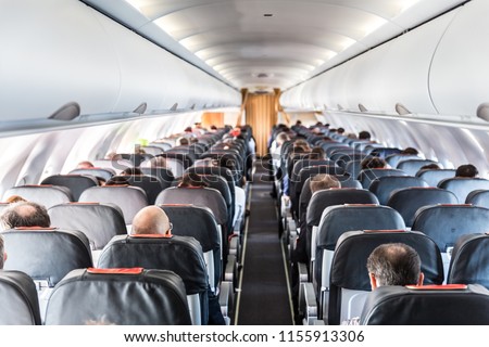Interior of commercial airplane with unrecognizable passengers on their seats during flight shot from the rear of airplane.