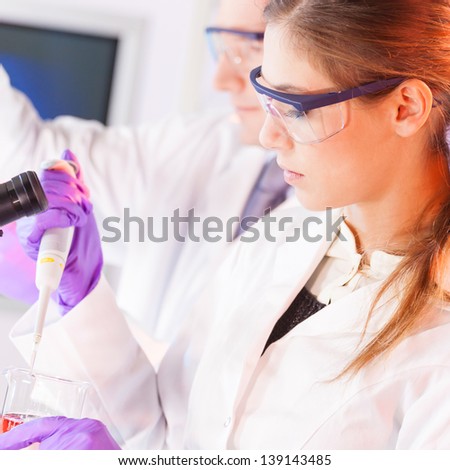 Chemical laboratory scene: attractive young scientist pipetting  red indikator solution.