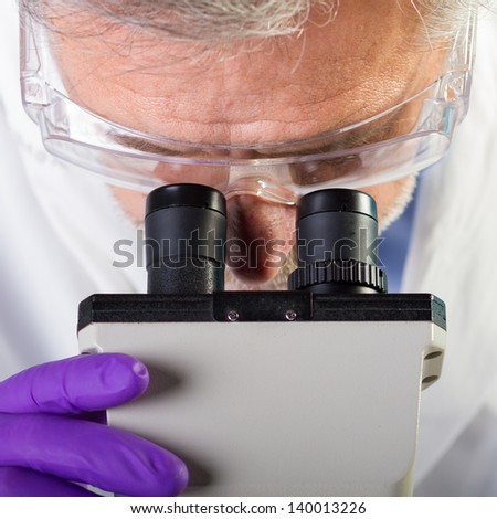 Focused senior life science professional routine screening the microscope slides in the cell laboratory. Lens focus on the researcher's face.