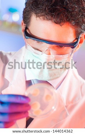 Mask protected life science professional observing the petri dish. Focus on scientist\'s eye.