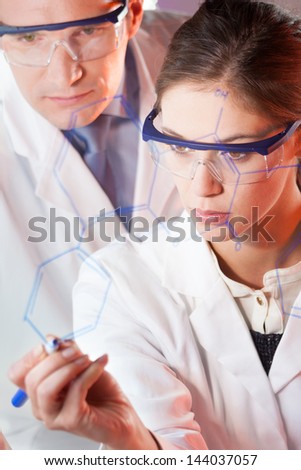 Portrait of a focused health care professionals in their working environment writing structural chemical formula on a glass board.