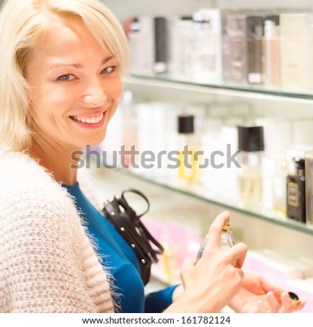 Cheerful elegant blond young woman testing cosmetics in perfumery.
