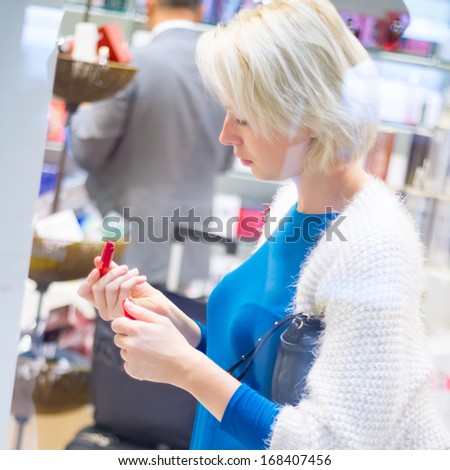 Casual blond young woman buying red lipstick in duty free shop on the airport.