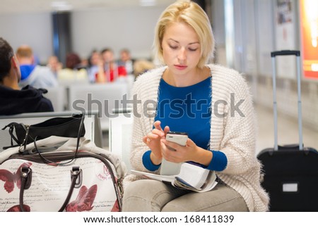 Casual blond young woman using her cell phone while waiting to board a plane at the departure gates Casual blond young woman using her cell phone while waiting to board a plane at the departure gates