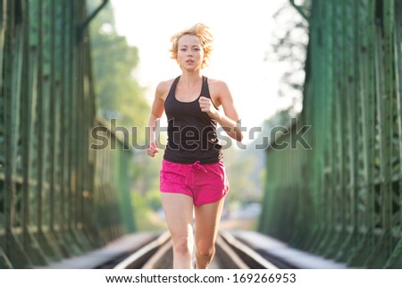 Athlete running on railaway tracks bridge in morning sunrise training for marathon and fitness. Healthy sporty caucasian woman exercising in urban environment; Active urban lifestyle.