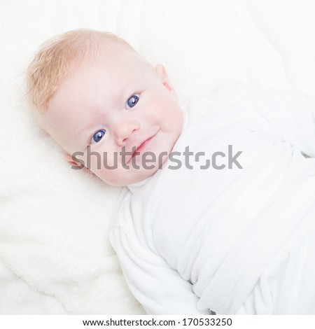 Cute blonde little baby boy with blue eyes smiling.