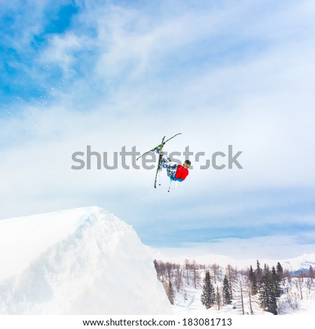 Free style skier performing a high up in the sky back flip jump. Snow covered mountains in the background.