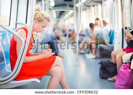 Beautiful blonde caucasian lady in red dress traveling by metro.