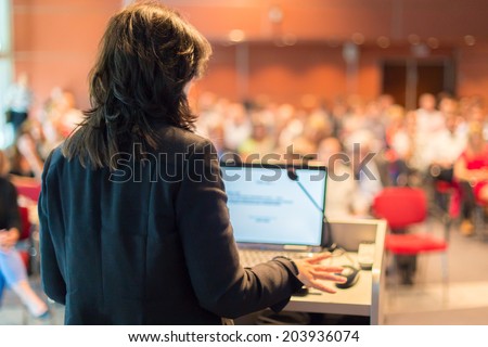 Business woman lecturing at Conference. Audience at the lecture hall.