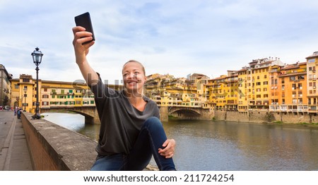 Young lady taking selfie in front of Ponte Vecchio bridge in Florence Tuscany Italy, during her summer vacations in Europe.