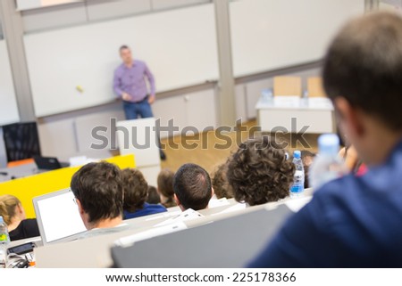 Professor giving presentation in lecture hall at university. Participants listening to lecture and making notes.