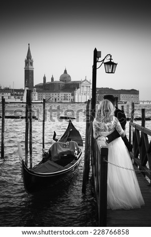 Romantic married couple in Romantic Italian city of Venice in black and white. Traditional Venetian wooden gondola and Roman Catholic church of San Giorgio Maggiore in the background.