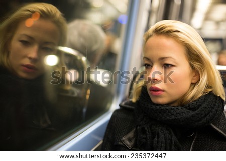 Thoughtful lady riding on a subway and looking out the window. Reflection of her face can be seen in the window.