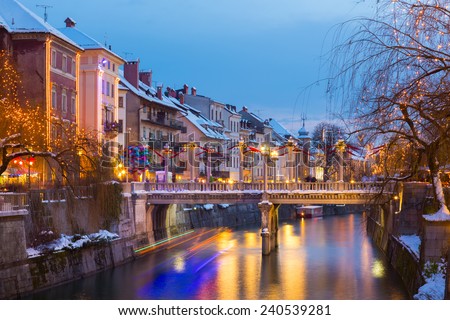View of lively river Ljubljanica bank with Cobblers\' Bridge in old city center decorated with Christmas lights. Ljubljana, Slovenia, Europe. Shot at dusk.