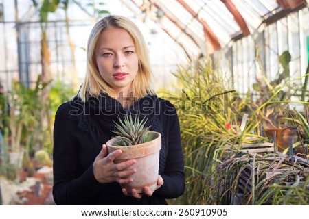 Portrait of florists woman working with flowers in a greenhouse holding a pot plant in her hand. Small business owner.