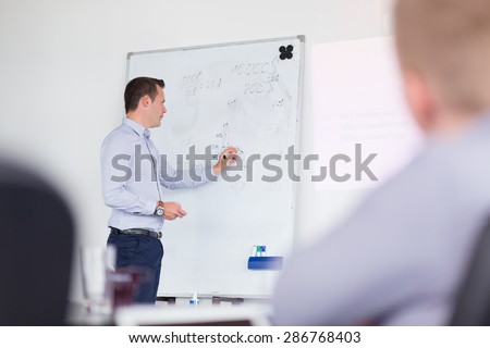 Businessman writing on whiteboard during his presentation on in-house business training, explaining business plans to his employees.