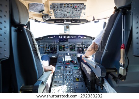 Rear view of pilot and copilot flying comercial airplane. Interior of airplane cockpit. Instrument panels in pilot\'s cabin.