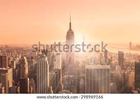 New York City. Manhattan downtown skyline with illuminated Empire State Building and skyscrapers at sunset. Vertical composition. Warm evening colors. Sunbeams and lens flare.