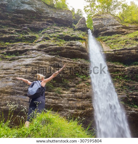 Female hiker raising arms inhaling fresh air, feeling relaxed and free in beautiful natural environment under Pericnik waterfall in Vrata Valley in Triglav National Park in Julian Alps, Slovenia.