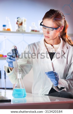 Life scientists researching in laboratory. Focused female life science professional pipetting blue solution into glass cuvette. Lens focus on researcher's eyes. Healthcare and biotechnology concept.