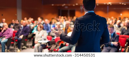 Speaker at Business Conference with Public Presentations. Audience at the conference hall. Entrepreneurship club. Rear view. Panoramic composition. Background blur.