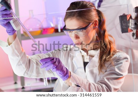 Life scientists researching in laboratory. Focused female life science professional pipetting solution into the glass cuvette. Lens focus on researcher's eyes. Health care and biotechnology concept.