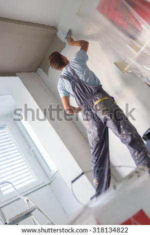 Thirty years old manual worker with wall plastering tools inside a house. Plasterer renovating indoor walls and ceilings with float and plaster.