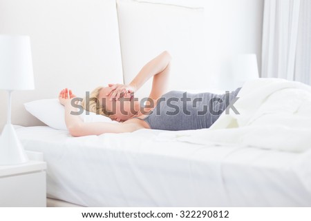 Still sleepy and tired young beautiful woman refuses to wake up and get of the bad in morning. Lack of sleep concept.  Horizontal composition