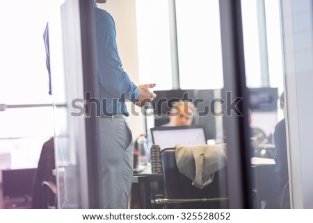Business man making a presentation at office. Business executive delivering a presentation to his colleagues during meeting or in-house business training. View through glass.