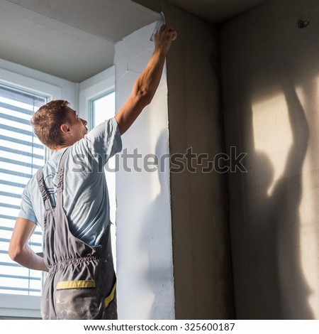 Thirty years old manual worker with wall plastering tools inside a house. Plasterer renovating indoor walls and ceilings with float and plaster.