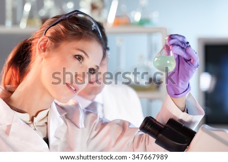 Chemical laboratory. Attractive young PhD student and her post doctoral supervisor scientist observing the blue indicator color shift after the solution  destillation.