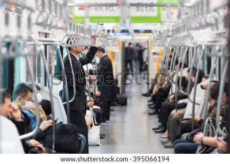 Passengers traveling by Tokyo metro. Business people commuting to work by public transport in rush hour. Shallow depth of field photo.