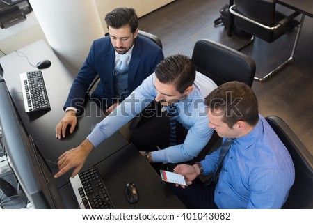 Businessmen trading stocks. Stock traders looking at graphs, indexes and numbers on multiple computer screens. Colleagues in discussion in traders office. Business success concept.