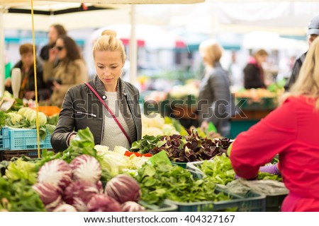 Woman buying fruits and vegetables at local food market. Market stall with variety of organic vegetable.